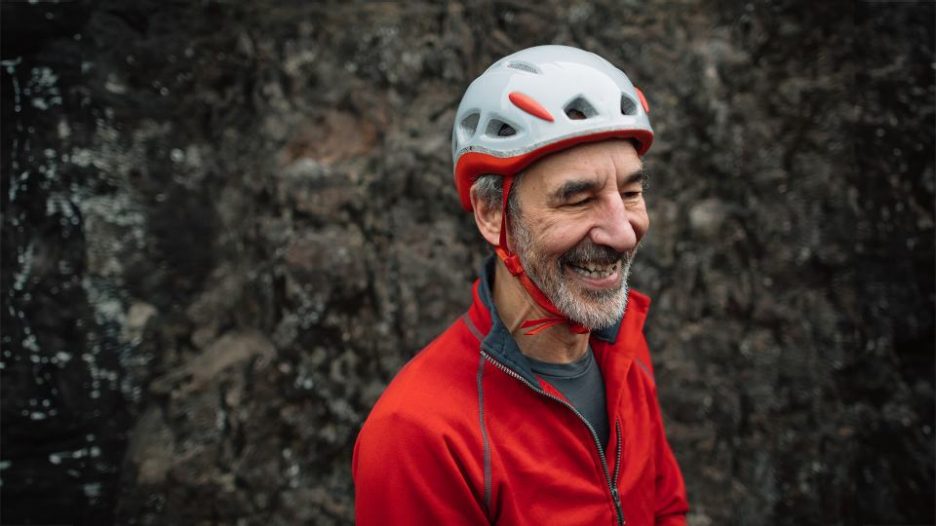 smiling older man wearing climbing helmet and red jacket