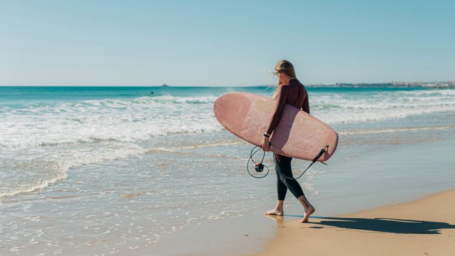 woman with a surfboard going into water during sunny day