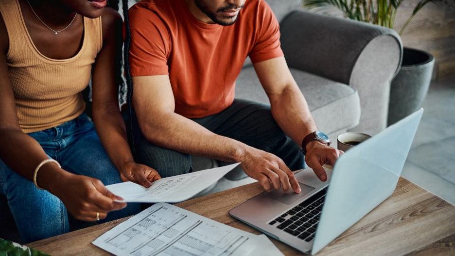 close up of a couple sitting on a grey sofa and using a laptop while reviewing their bills