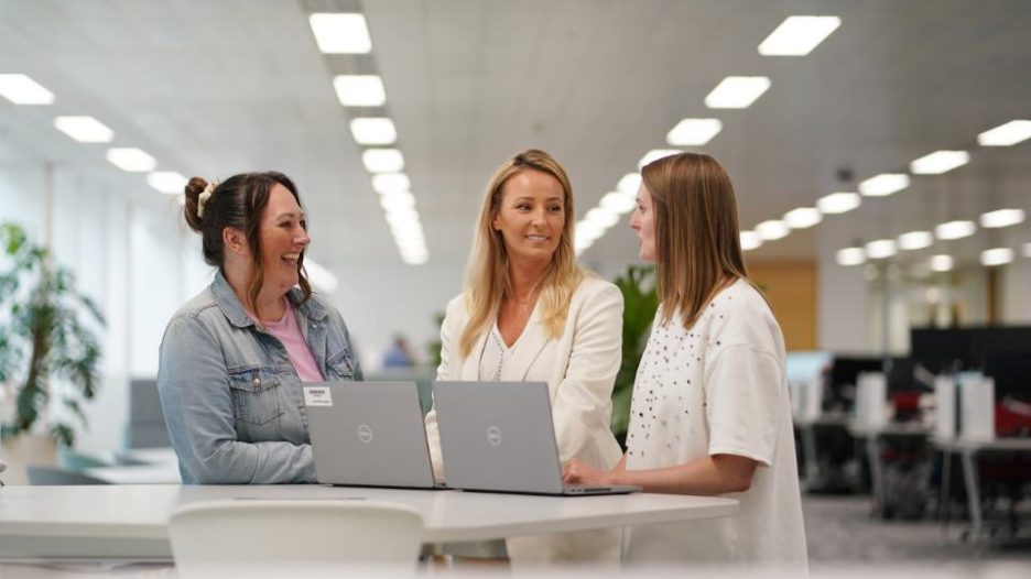 3 female Aegon employees standing at table around laptop