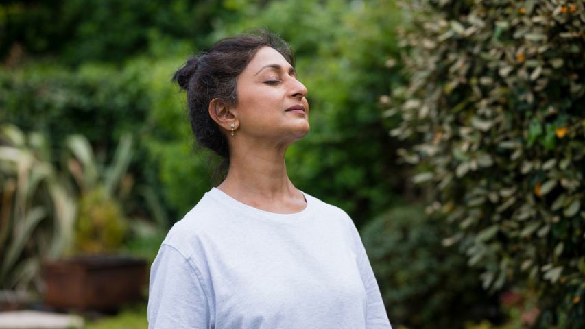 woman pausing to breathe and enjoy nature while standing in a large garden