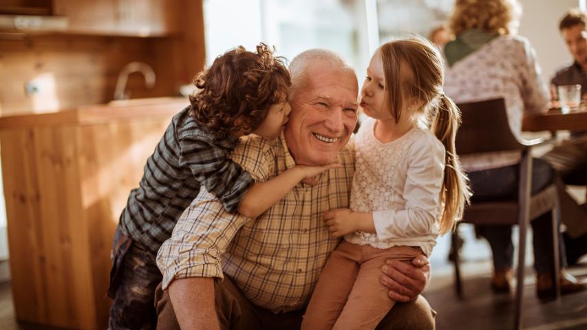 grandfather enjoying hugs from his young grandchildren with parents seated in the background