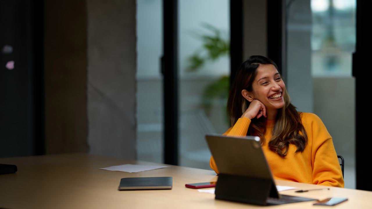 female worker in bright pullover laughing at her desk in office