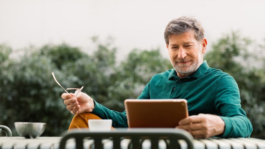 man sitting outdoors drinking coffee and using digital tablet