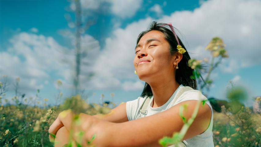 smiling woman sitting in field with yellow flowers