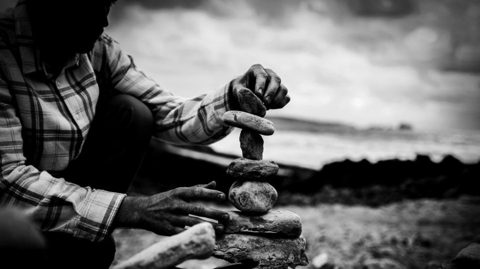 black and white image of man balancing stones stack on beach