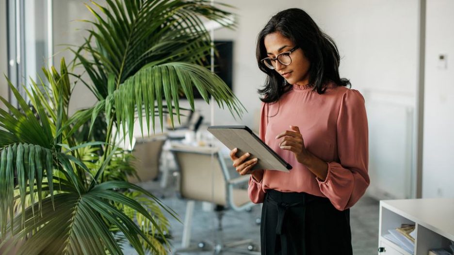 Female holding and looking at tablet in office area with large plant