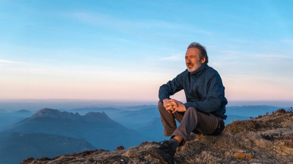 A man is sitting on the ground and looking at the setting sun.