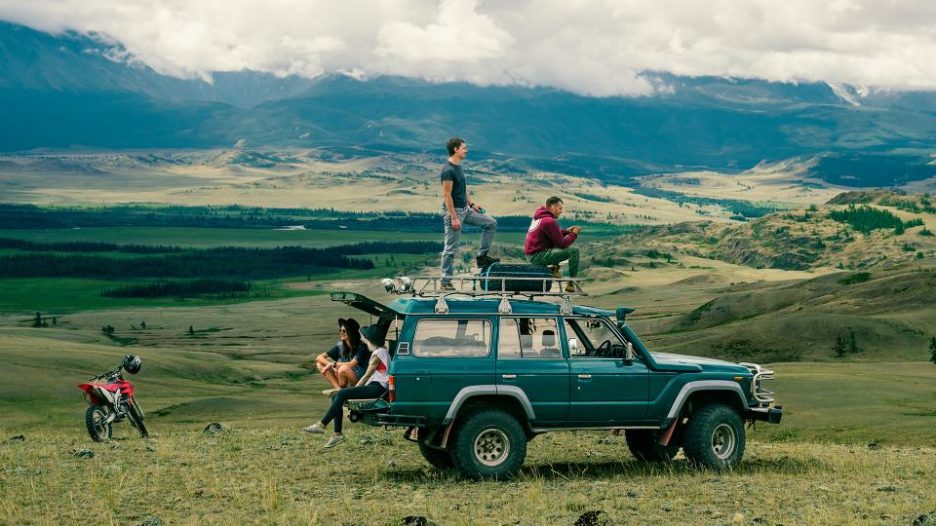 a group of four young friends sitting on an off road vehicle in a field in the countryside